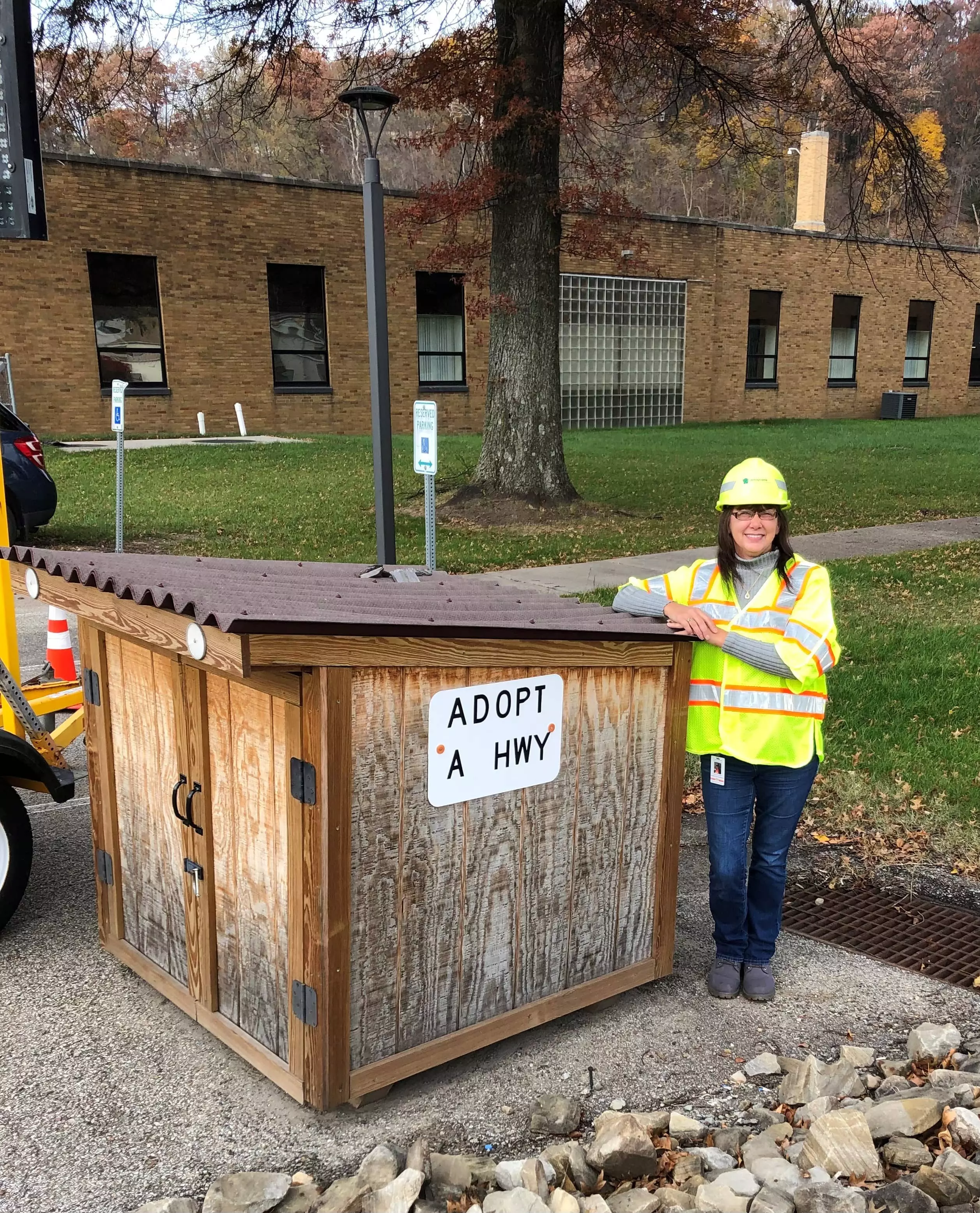An employee stands next to a small shed serving as the Adopt A Highway supply pick-up box.